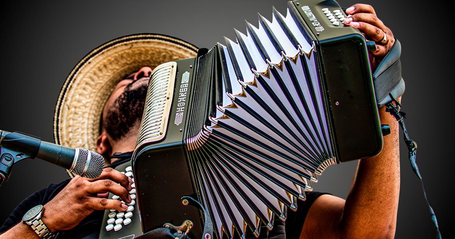 Acordeonero con sombrero tocando su acordeón frente al micrófono